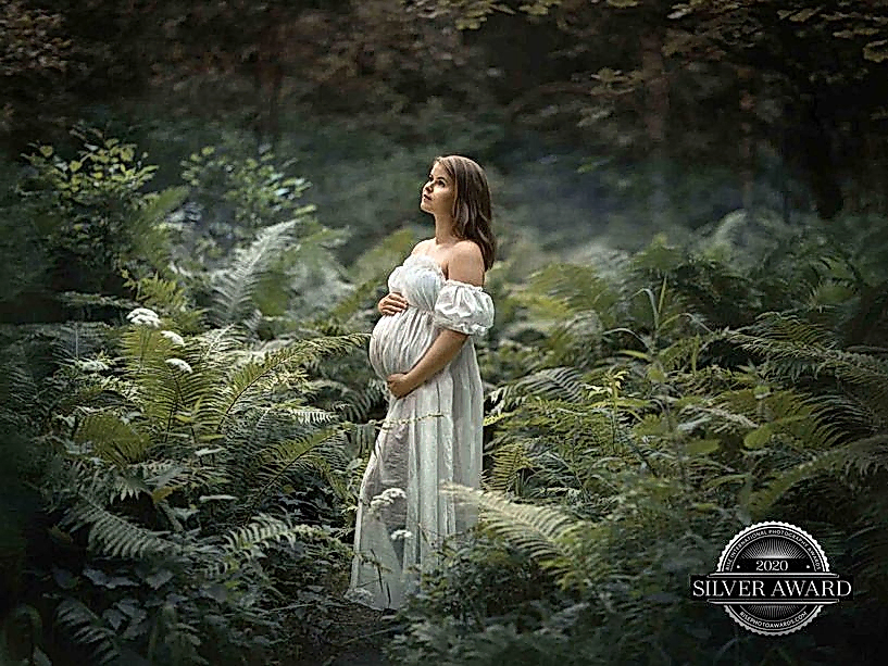 Gravid kvinne med hvit kjole blandt bregner